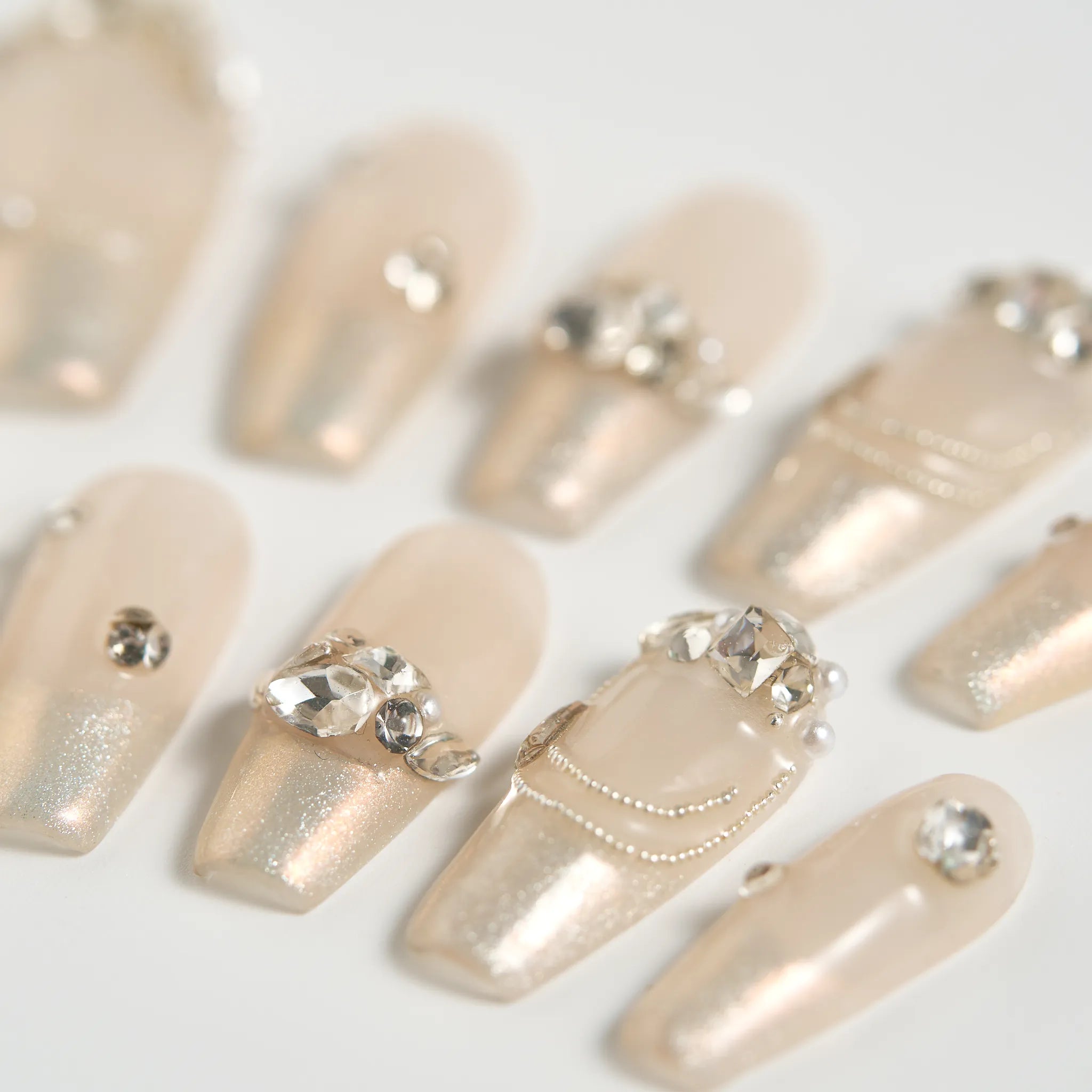 Beige nail art designs with rhinestones on a white background