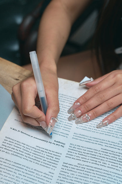 Person with Gilded Heiress rhinestone press-on nails writing on a document with a pen.