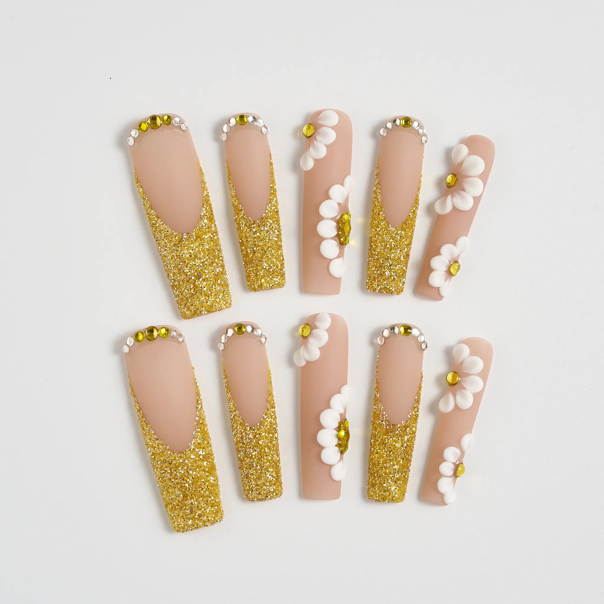 Set of false nails with gold glitter and white flower decorations on a light gray background