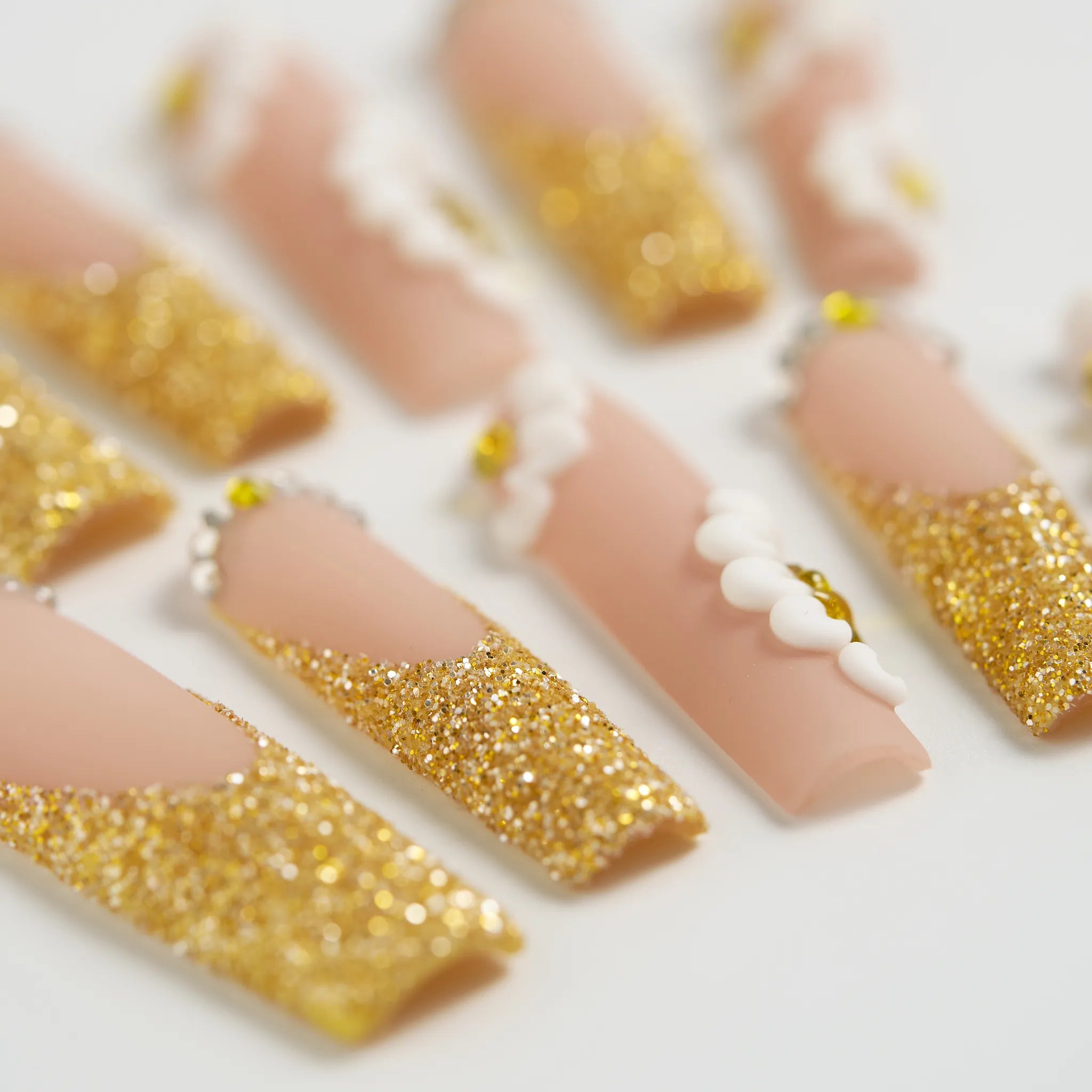 Nail art with gold glitter and white accents on a light background