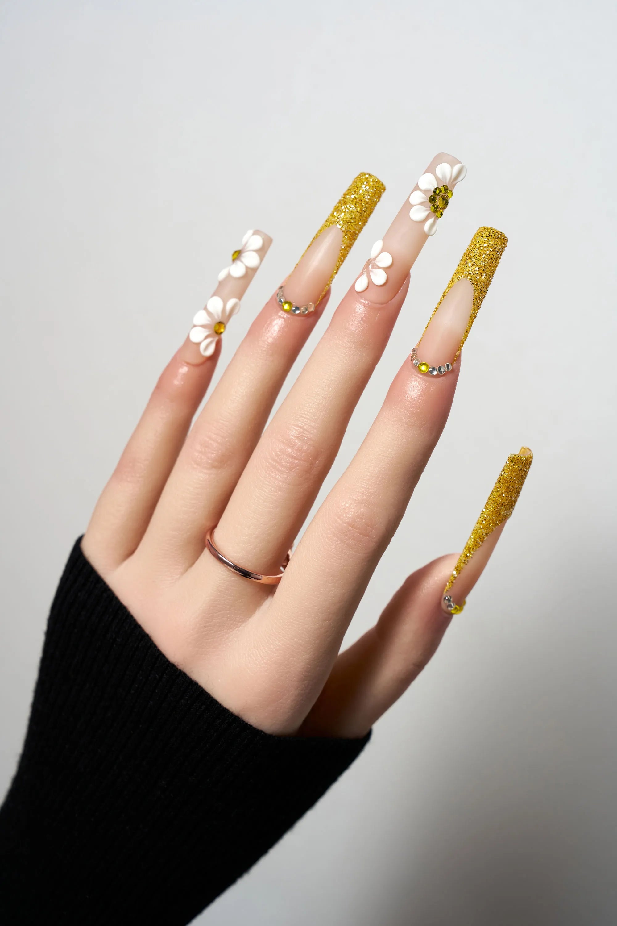 Golden Bloom reusable extra-long coffin press-on nails featuring gold glitter French tips, decorated with 3D white daisy flowers with amber centers and delicate crystal borders.