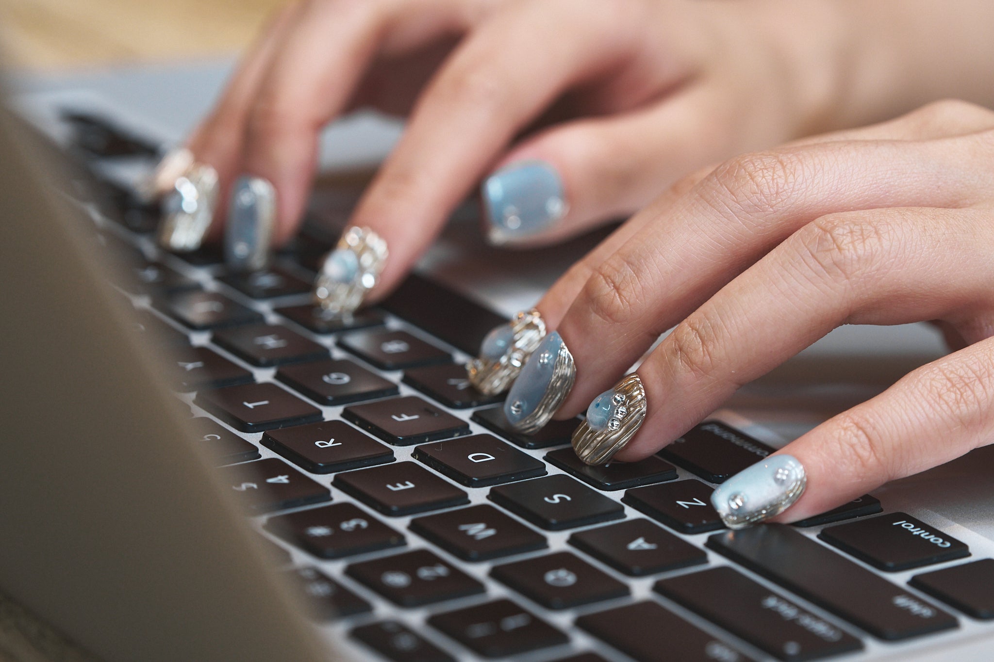 Close-up of hands wearing Mist Orbit press-on nails typing on a laptop keyboard.