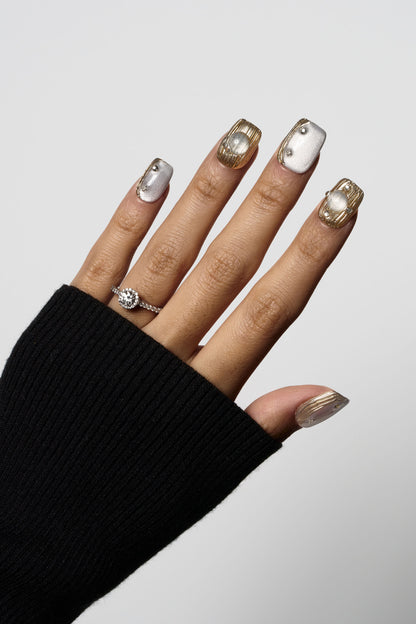Mist Orbit press-on nails showcasing a silvery grey cat-eye effect combined with 3D textured gold metallic designs and small pearl embellishments.
