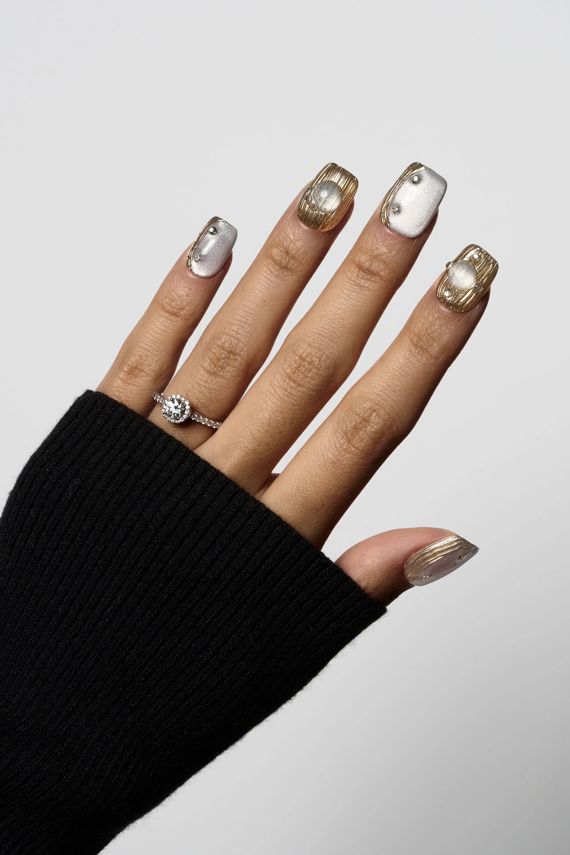 Mist Orbit press-on nails showcasing a silvery grey cat-eye effect combined with 3D textured gold metallic designs and small pearl embellishments.