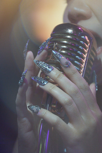 MiuNail Chrome Reign metallic nail extensions, dramatic silver gothic nail art, holding a vintage microphone, live performance aesthetic.