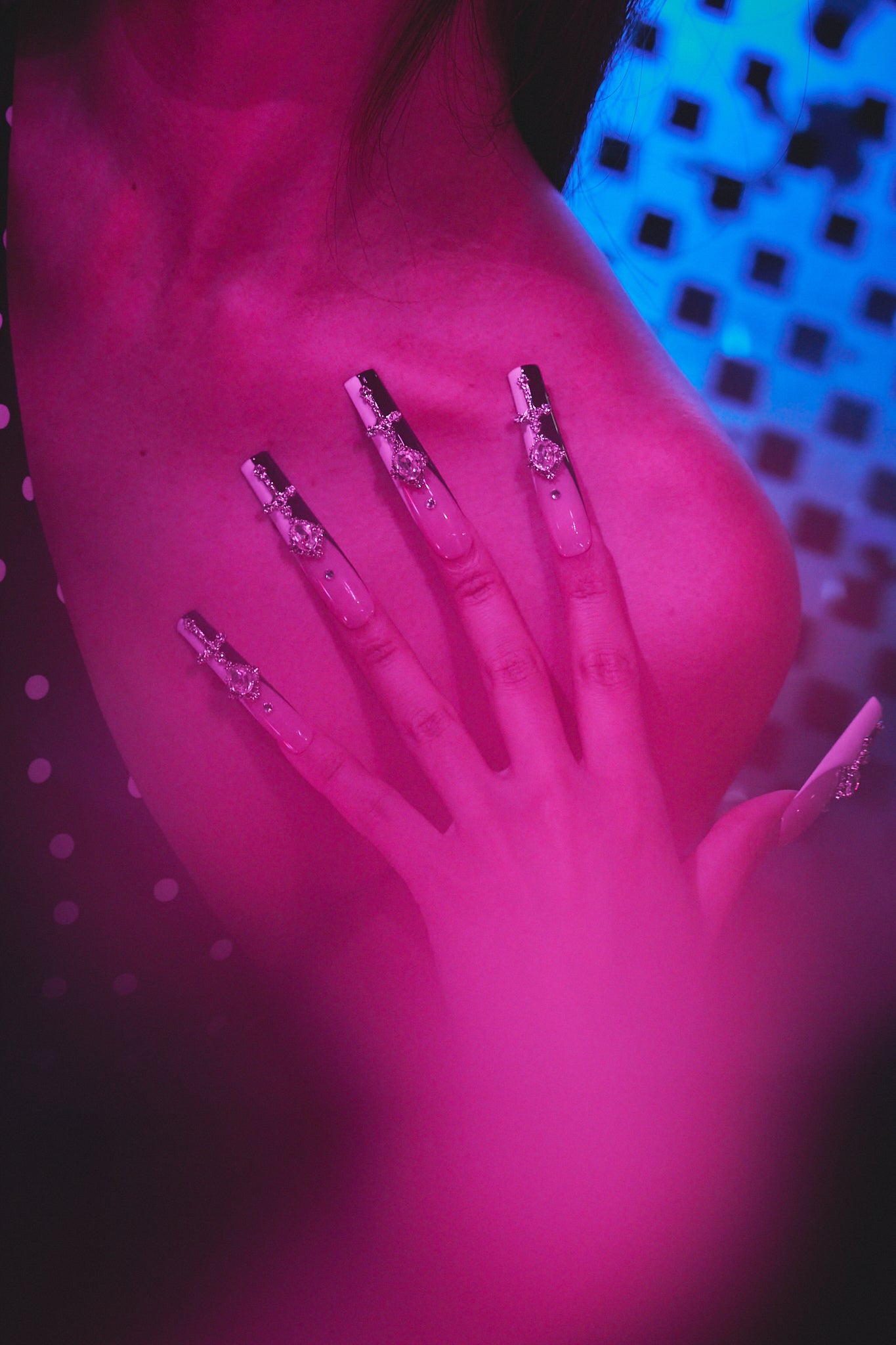 Hand wearing MiuNail Divine Plea black and white cross press-on nails resting on chest, under dramatic purple and blue lighting with soft polka dot elements.