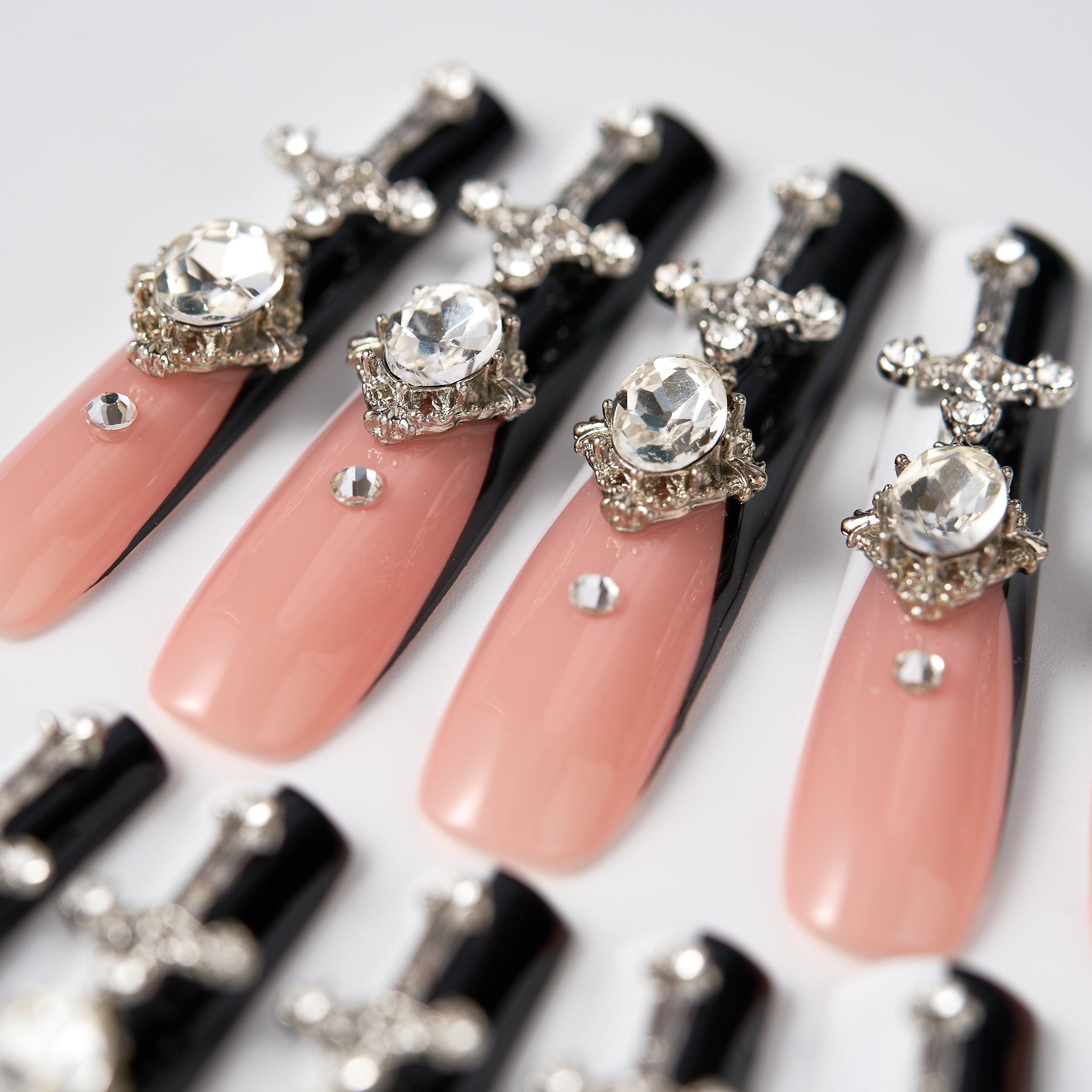 Semi-close view of Divine Plea press-on nails by MiuNail, showcasing nude pink and black nails with silver cross charms and rhinestone embellishments on a white background.