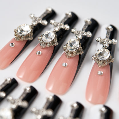 Semi-close view of Divine Plea press-on nails by MiuNail, showcasing nude pink and black nails with silver cross charms and rhinestone embellishments on a white background.