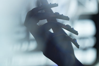 Silhouette of a hand wearing Divine Plea press-on nails by MiuNail, featuring gothic cross embellishments against a blurred monochrome background.