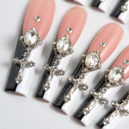 Angled close-up of Divine Plea press-on nails from MiuNail, featuring aligned silver cross charms, large rhinestones, and glossy black and white tips on a nude base over white background.