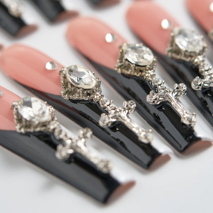 Macro close-up of MiuNail Divine Plea press-on nails, showcasing glossy black tips, nude base, and ornate silver cross charms with rhinestones on a white background.