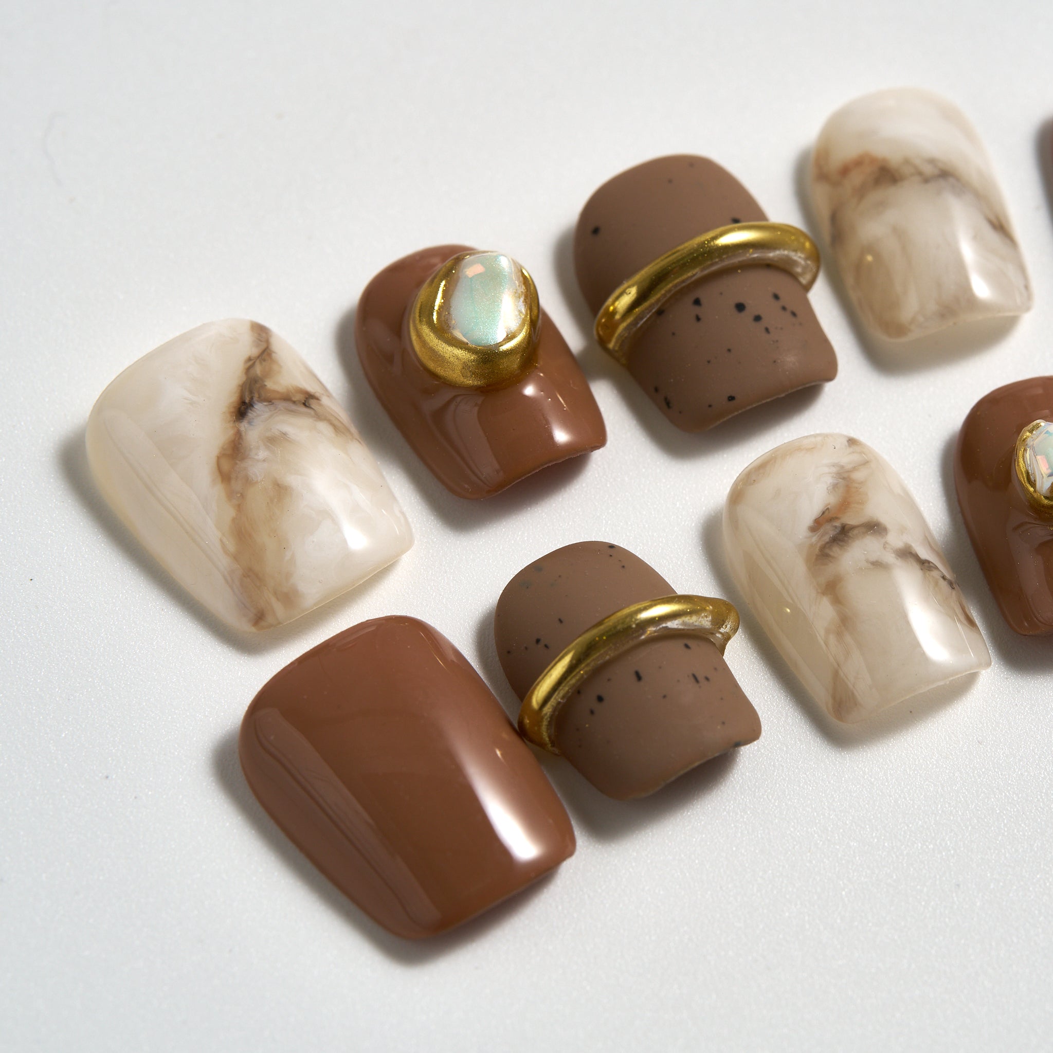 Close-up of MiuNail Golden Dune press-on nails featuring marble beige, taupe, and brown designs with metallic gold accents, displayed on a white background.