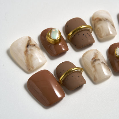 Close-up of MiuNail Golden Dune press-on nails featuring marble beige, taupe, and brown designs with metallic gold accents, displayed on a white background.