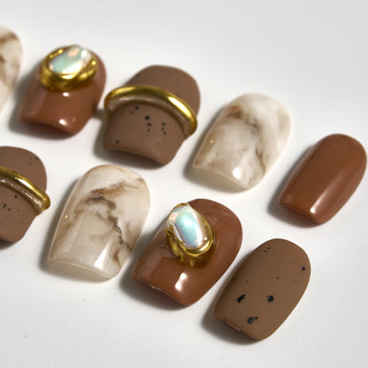 Close-up of MiuNail Golden Dune press-on nails featuring marble brown, taupe, and cream tones with gold metallic and pearl accents, displayed on a white background.