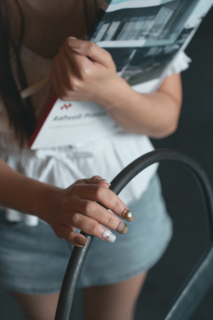 Person wearing MiuNail Golden Dune press-on nails with brown, marble, and gold accents, holding a newspaper and a handrail, with a blurred background.