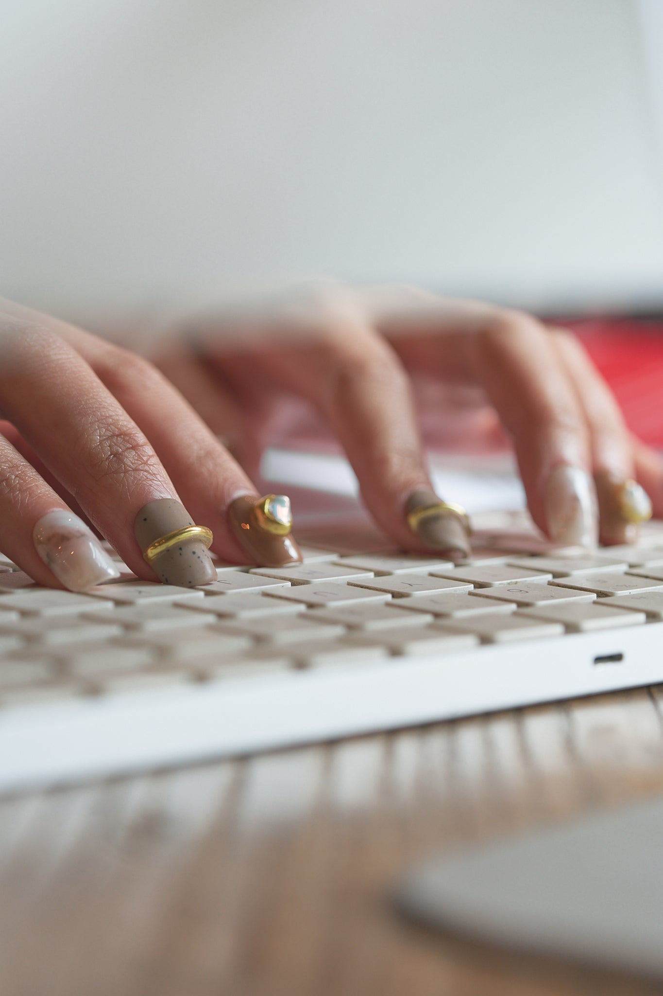 Hands wearing MiuNail Golden Dune press-on nails in marble, brown, and gold, typing on a white computer keyboard with a blurred background.