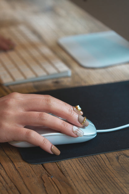 Hand wearing MiuNail Golden Dune press-on nails in marble and brown with gold accents, using a computer mouse on a wooden desk, keyboard in the background.