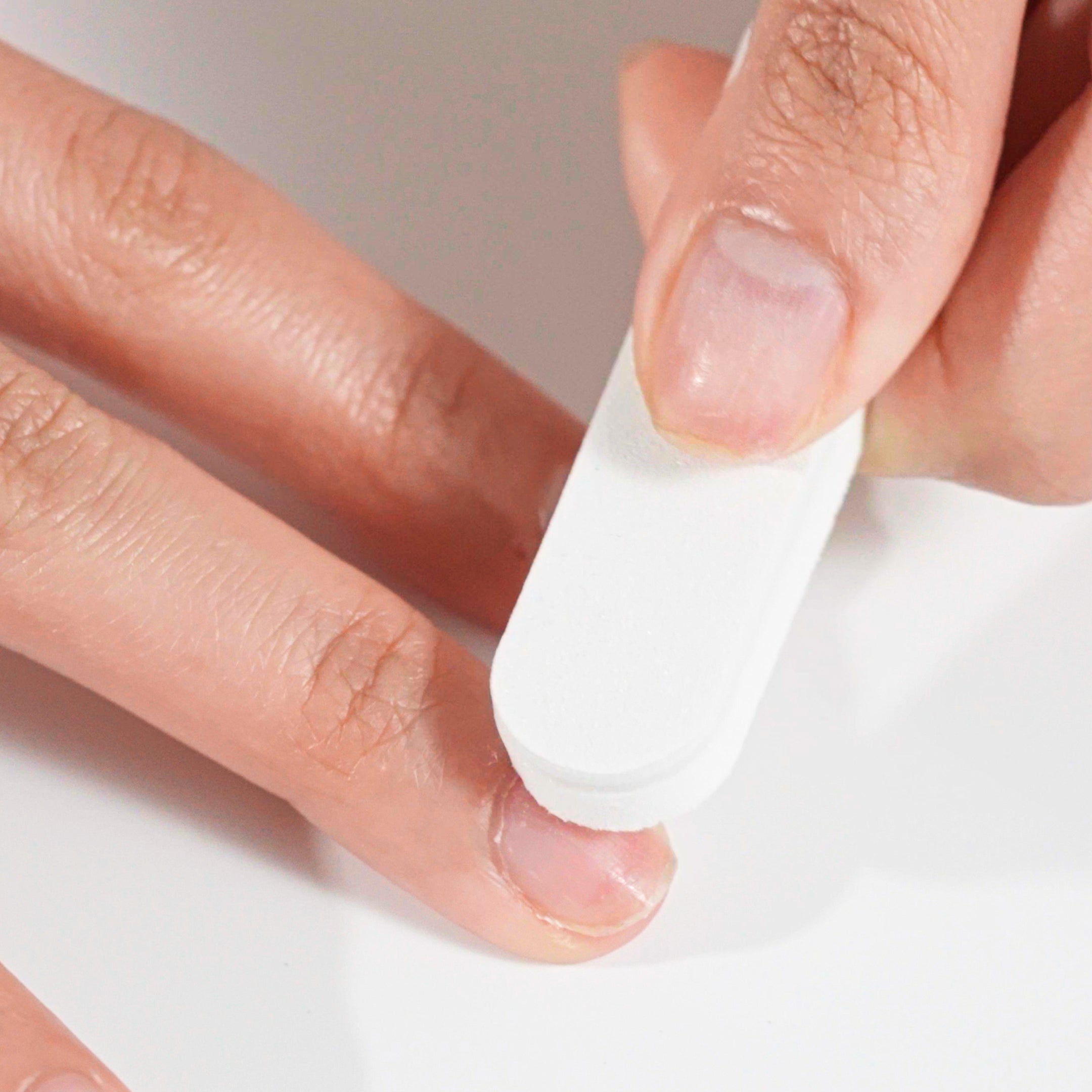 Close-up of a hand buffing the surface of a natural nail with a white nail buffer during press-on nail preparation.