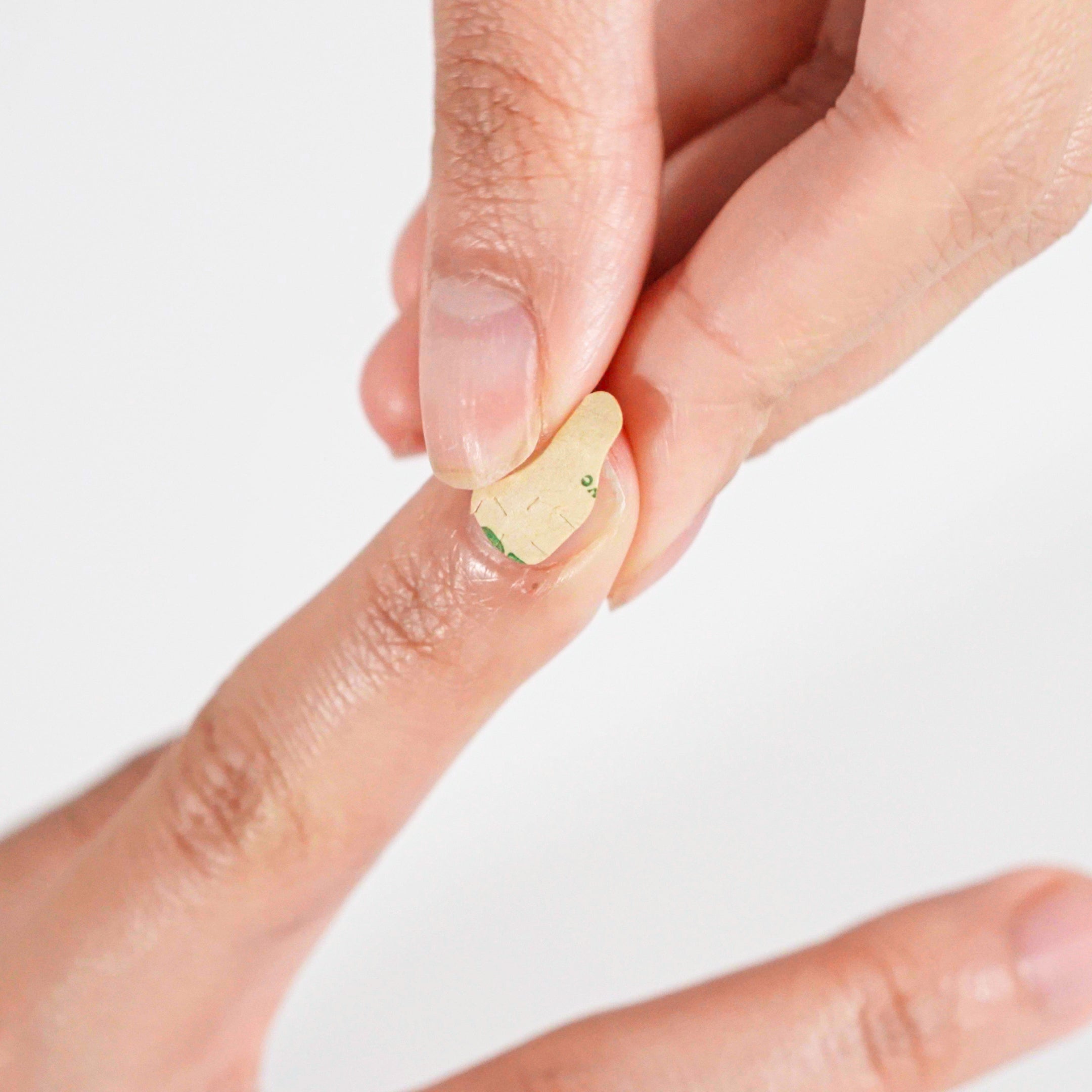 Close-up of a hand pressing adhesive onto the natural nail during press-on nail preparation.