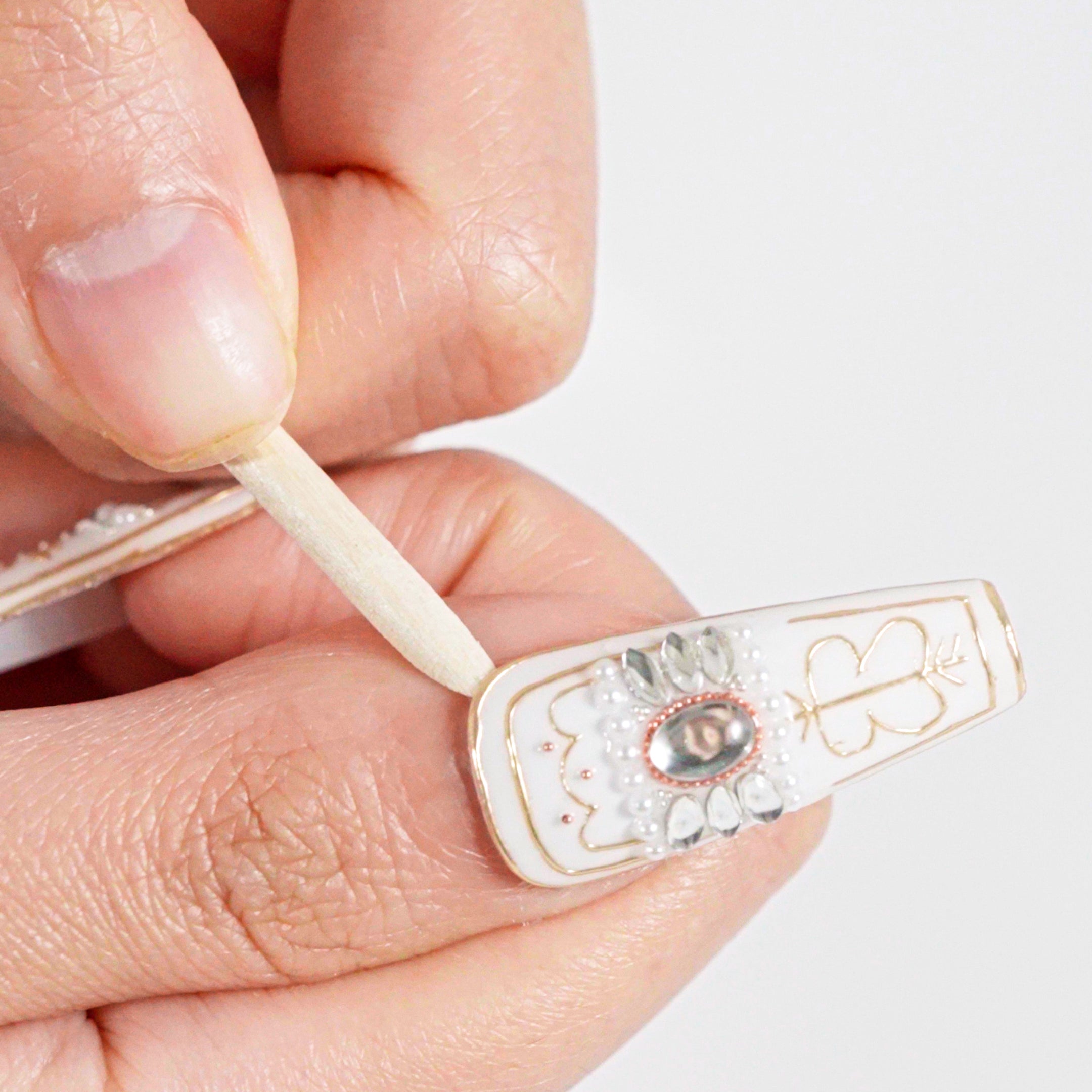 Close-up of a hand gently lifting the edge of a press-on nail with a manicure stick to begin removal.