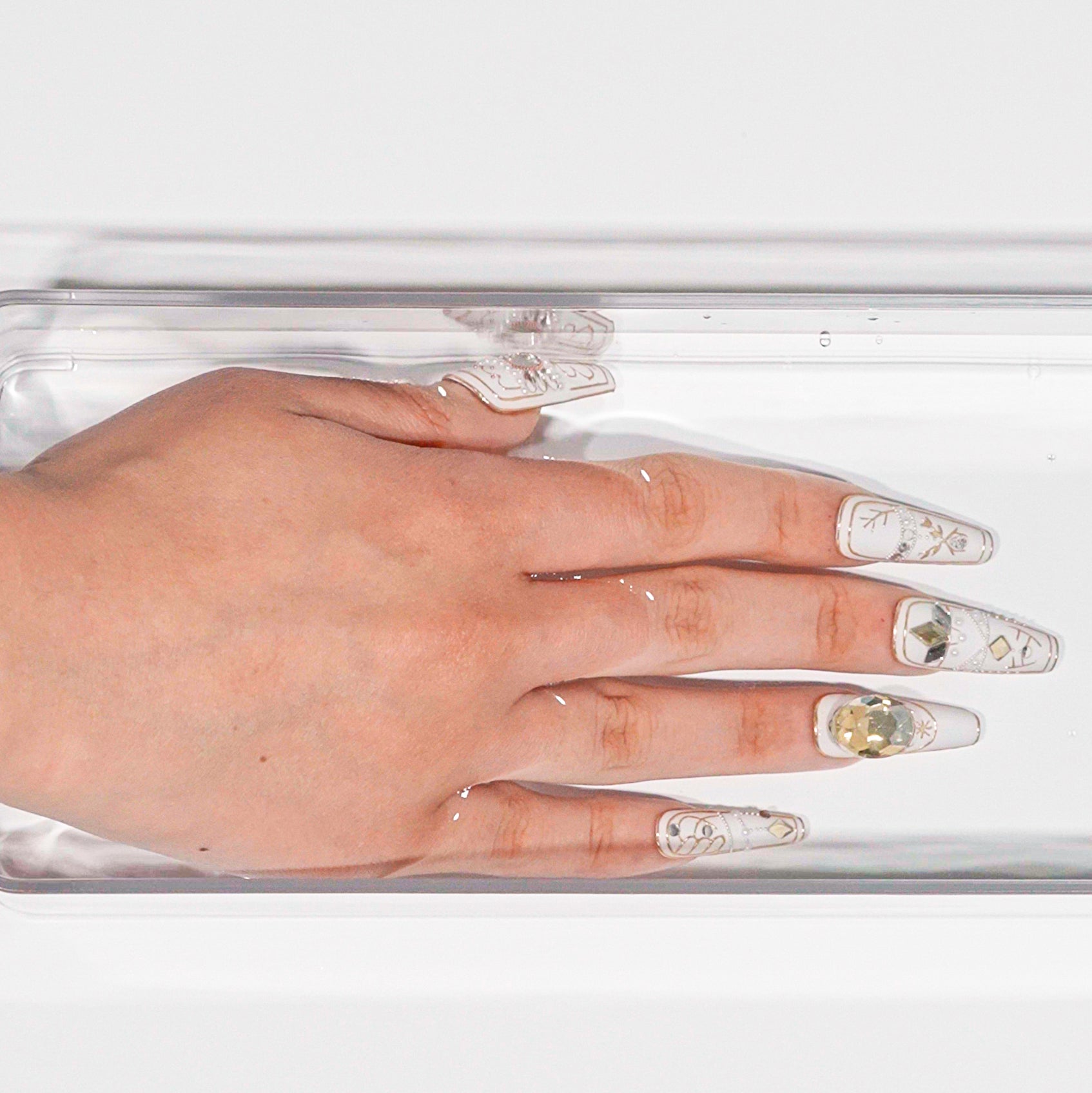 Close-up of fingers soaking in warm water to loosen adhesive during press-on nail removal.