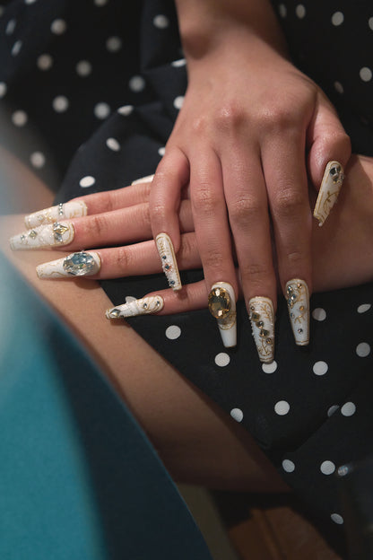 Both hands with gold-accented white nail art resting on a black polka dot dress, showing the complete manicure look.