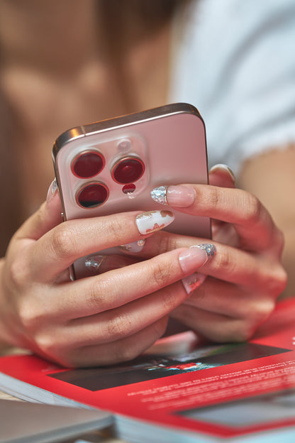 Petal Bloom long almond press-on nails in marble white and gold, hands holding a smartphone with blurred background