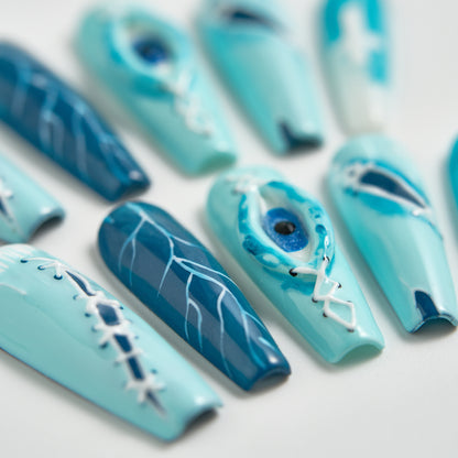 Angled close-up of MiuNail Siren Hex press-on nails in icy blue and navy with lightning veins, stitched designs, and a glossy eye detail, shown on a white surface.