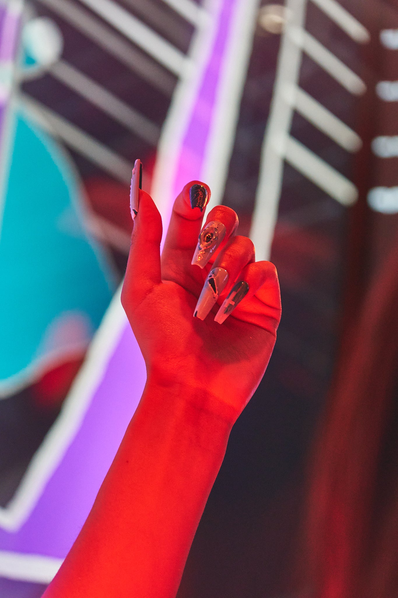 Raised hand wearing MiuNail Siren Hex press-on nails in black and blue, against a vibrant neon-lit background.