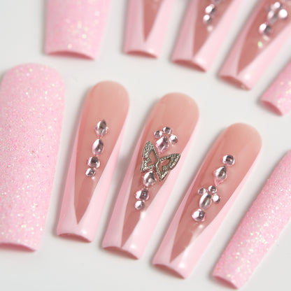Detailed view of pastel pink and nude press-on nails adorned with clear crystals and a butterfly charm, arranged on a clean white surface.