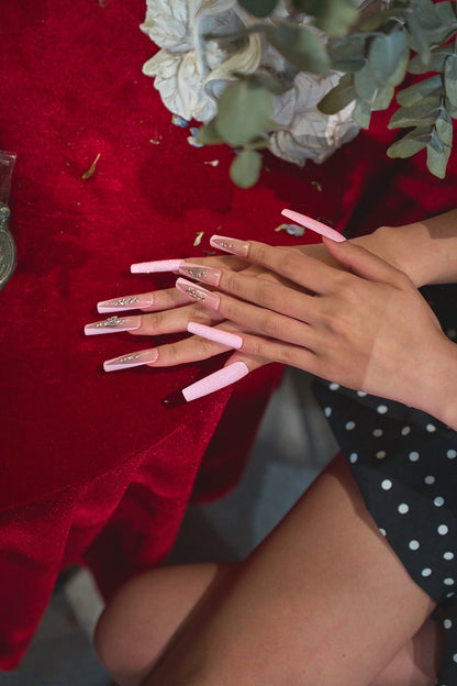 Hands with MiuNail Sugar Flutter pink press-on nails resting on a red velvet tablecloth, paired with a black polka dot dress.