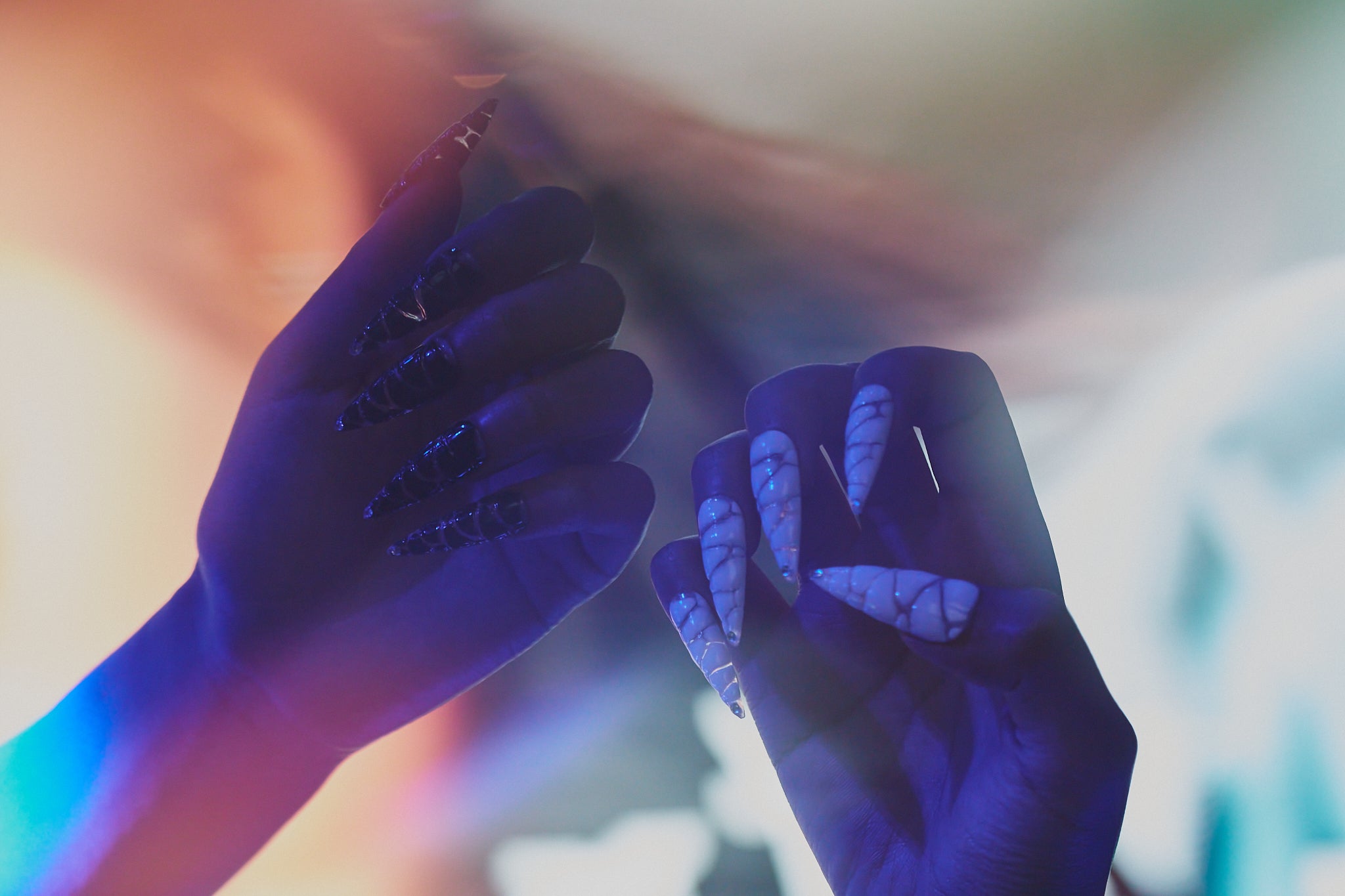 Two hands wearing MiuNail Venom Twist press-on nails—one in black, one in white—posed under iridescent lighting with soft color gradients.