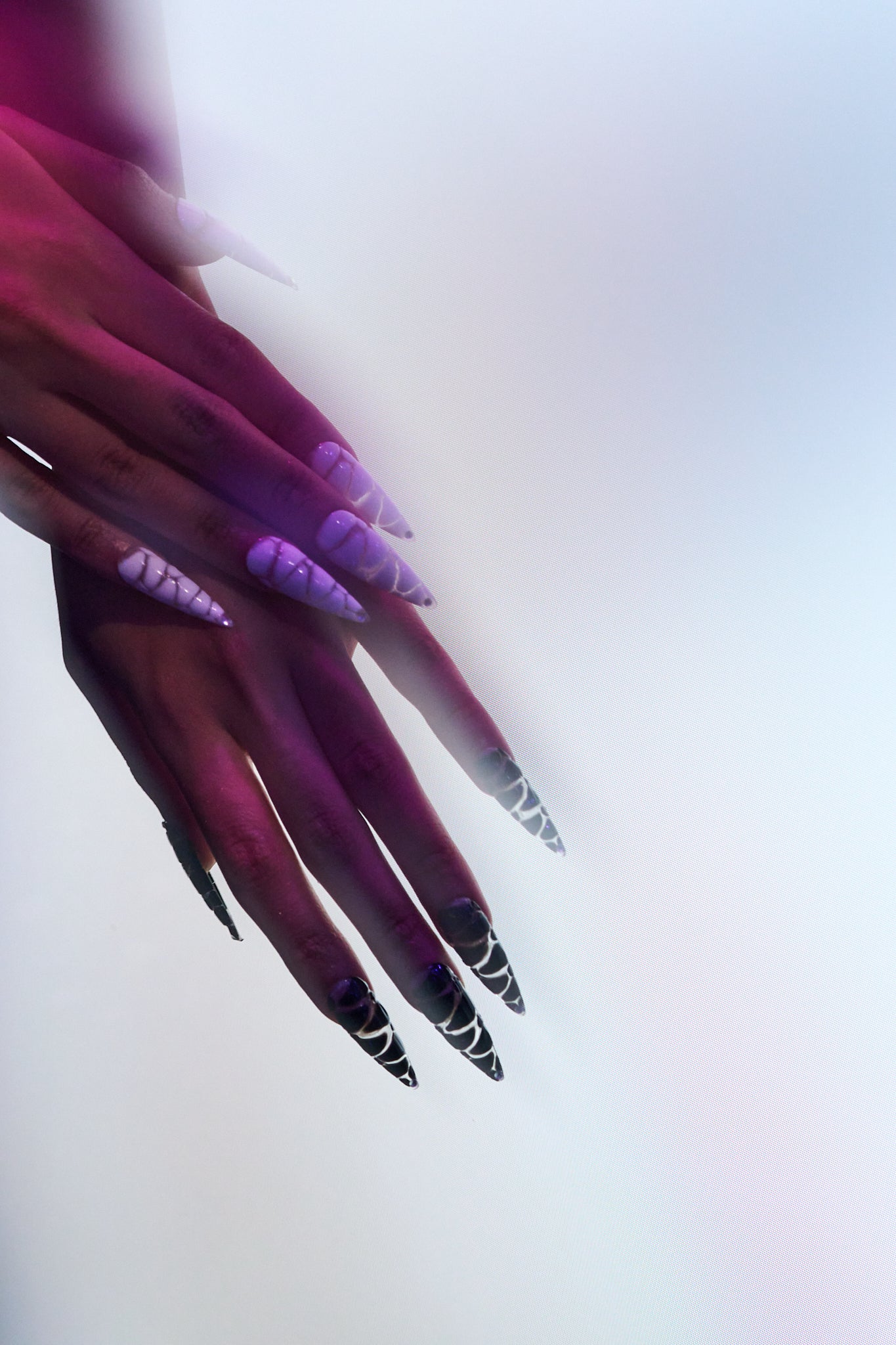 MiuNail Venom Twist nails in black and white, worn on both hands and captured under soft gradient lighting with purple hues.