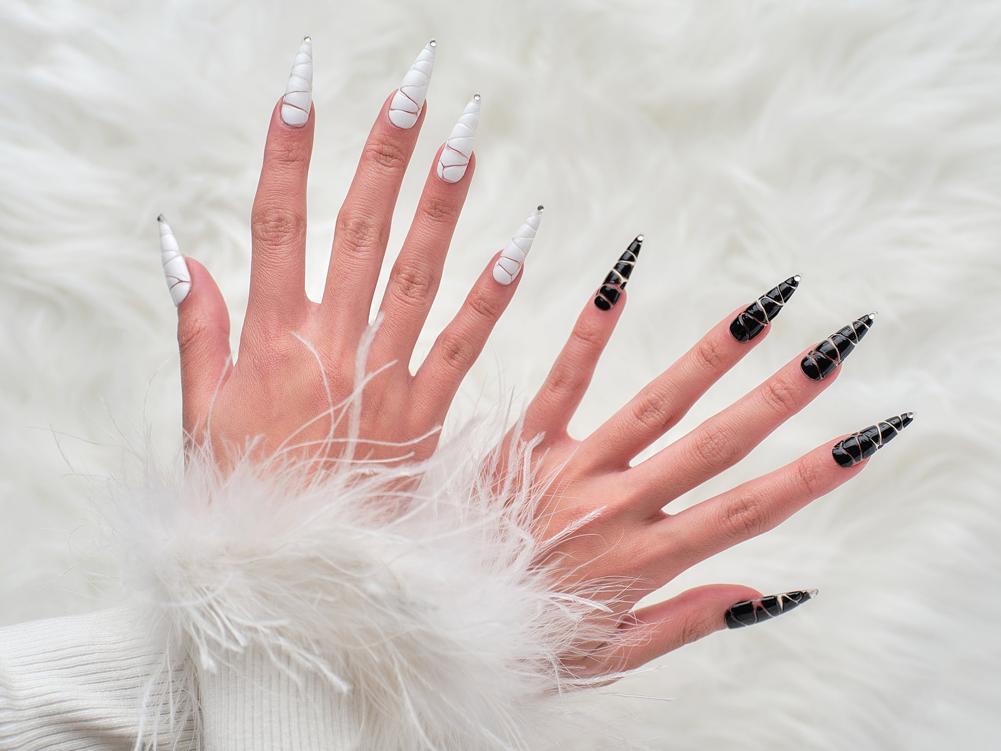 Hands wearing MiuNail Venom Twist press-on nails in black and white chrome spiral designs, shown against a soft fur background.