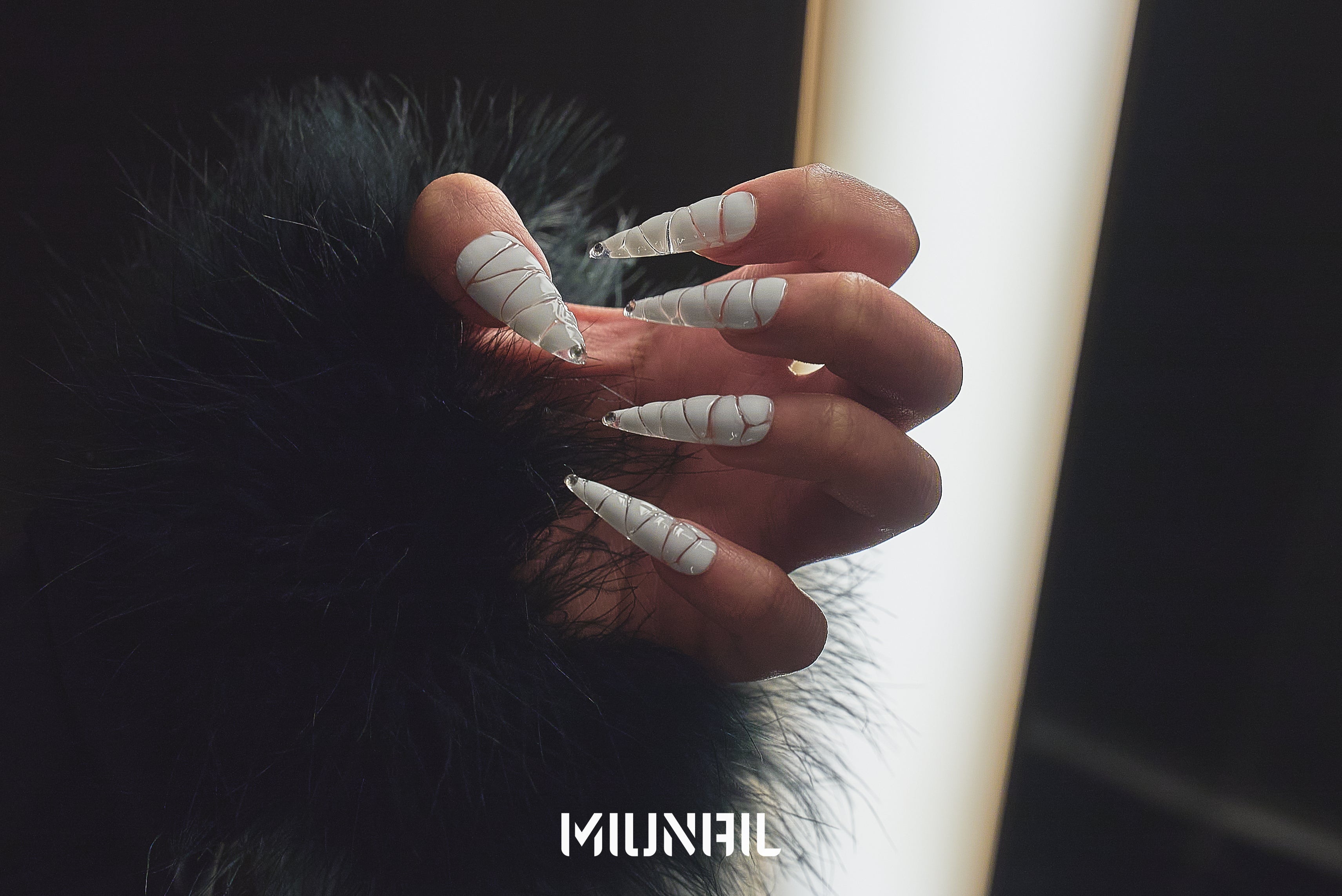 Hand wearing MiuNail Venom Twist white press-on nails with metallic spiral wraps, styled against a dark backdrop with faux fur sleeve.