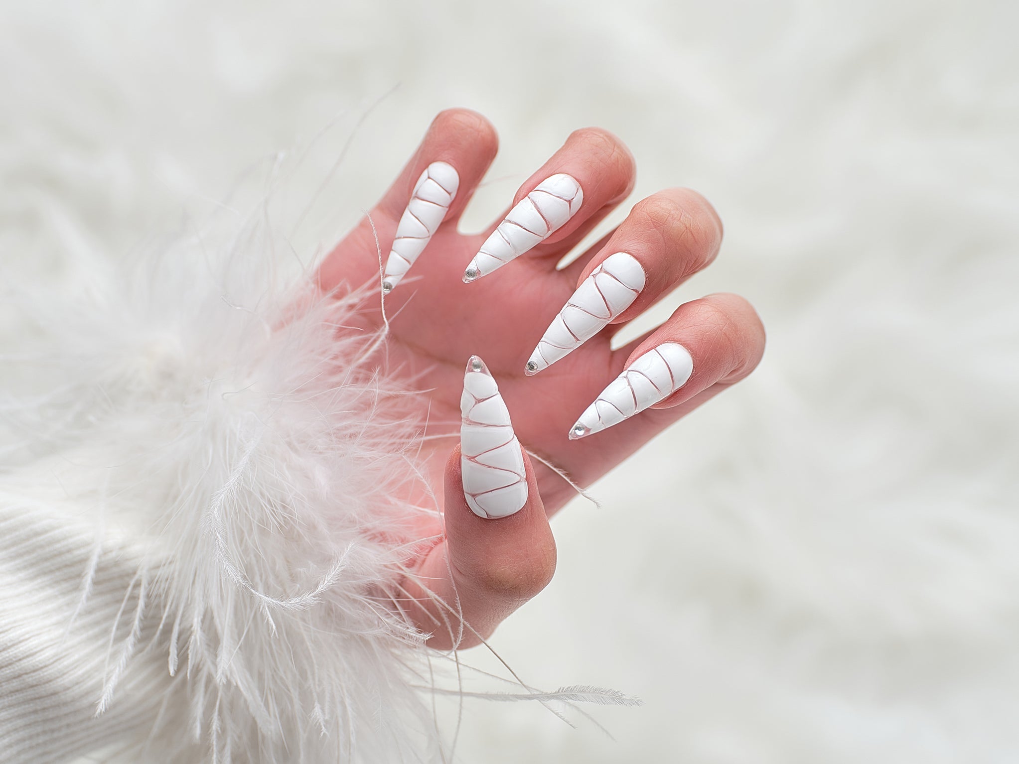 Hand wearing MiuNail Venom Twist white press-on nails with chrome spiral texture and pointed tips, shown against a soft white fur background.