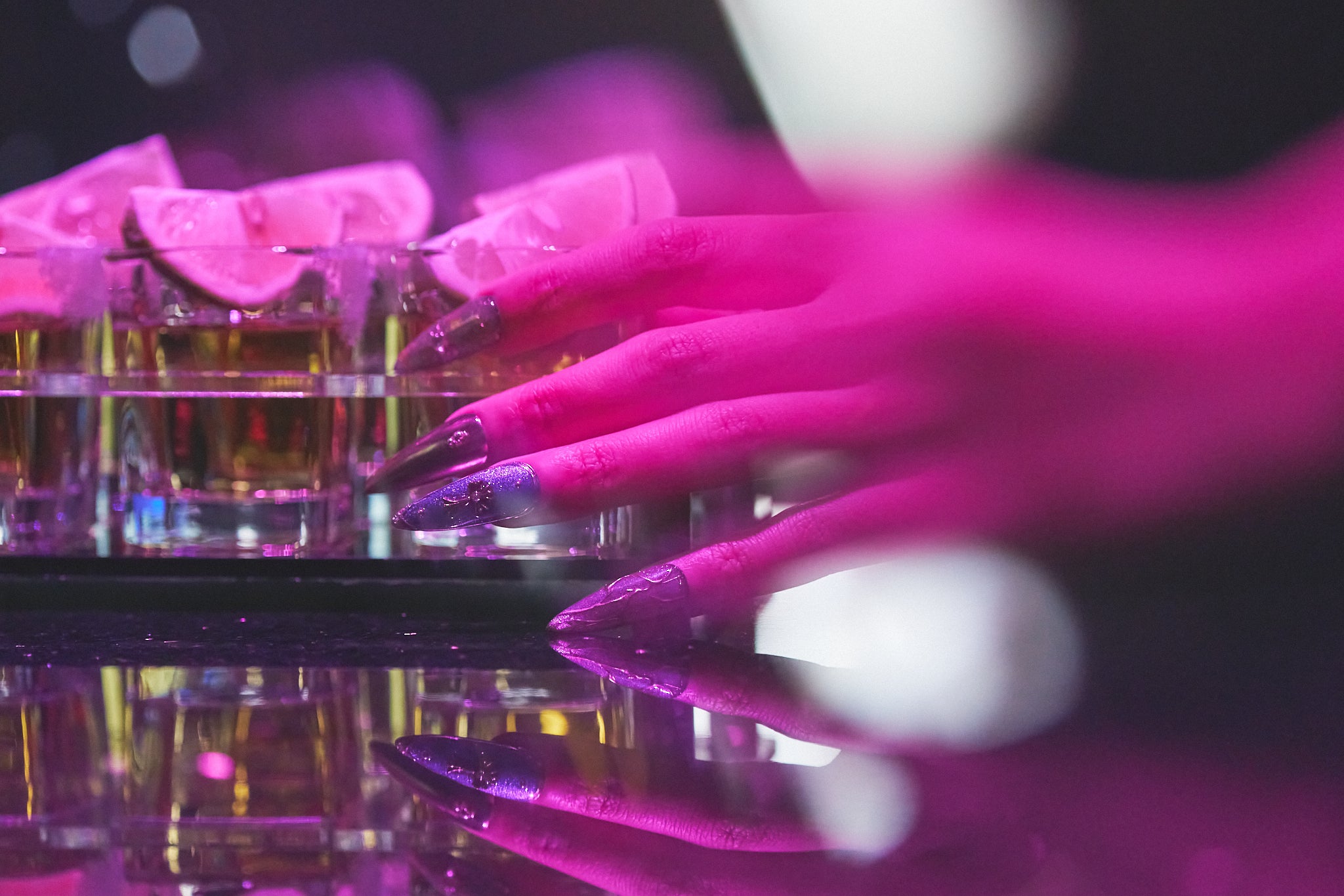 Violet Eclipse stiletto press-on nails in metallic purple and gold, hand reaching for a drink at a bar, salon-quality reusable nails