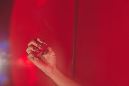 Violet Eclipse metallic purple and gold stiletto press-on nails, hand posed against a red background, instant manicure