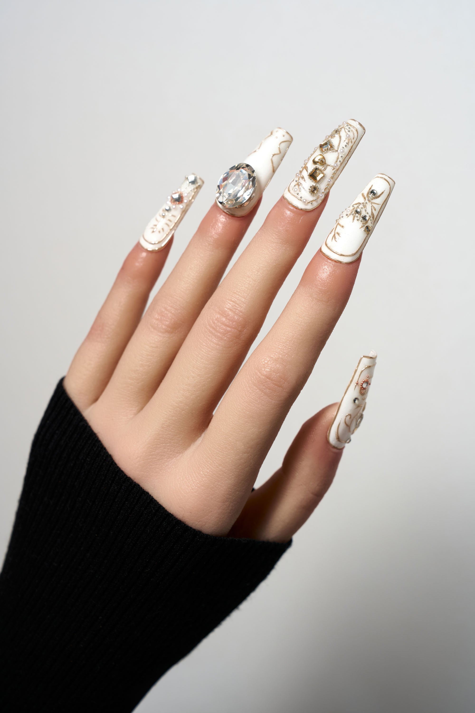 Ornate Veil medium coffin press-on nails in creamy white, featuring opulent gold embossed patterns, large focal gemstones, and intricate crystal and pearl decorations.