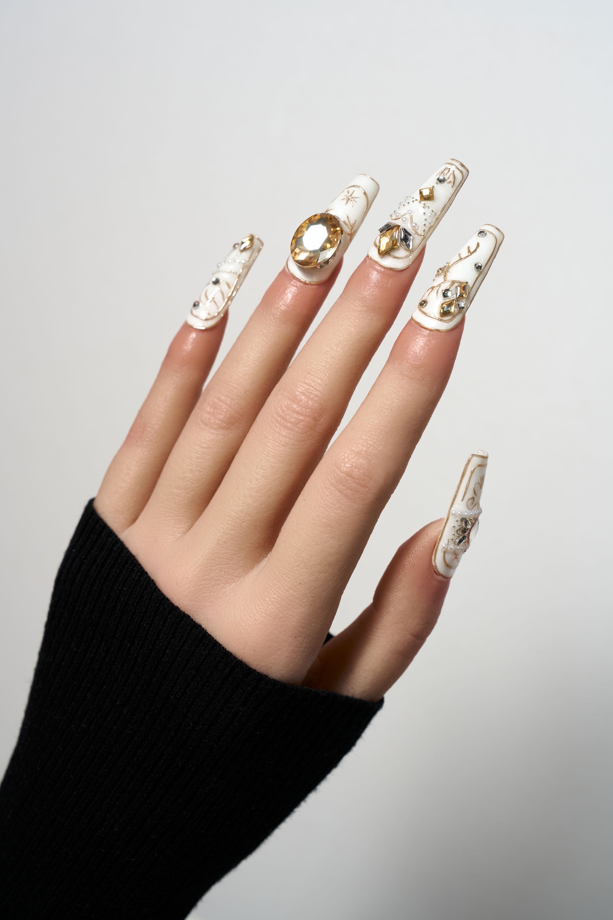 Ornate Veil medium coffin press-on nails in creamy white, featuring opulent gold embossed patterns, large amber gemstones, and intricate crystal decorations.