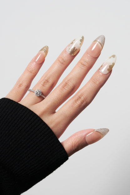 Petal Bloom almond-shaped press-on nails featuring elegant gold leaf floral art on a milky white base, paired with shimmering gold glitter French tips.