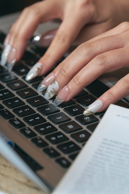 Hands adorned with delicate Petal Bloom nails gracefully typing on a laptop keyboard, soft focus on the background creating a cozy work-from-home vibe.