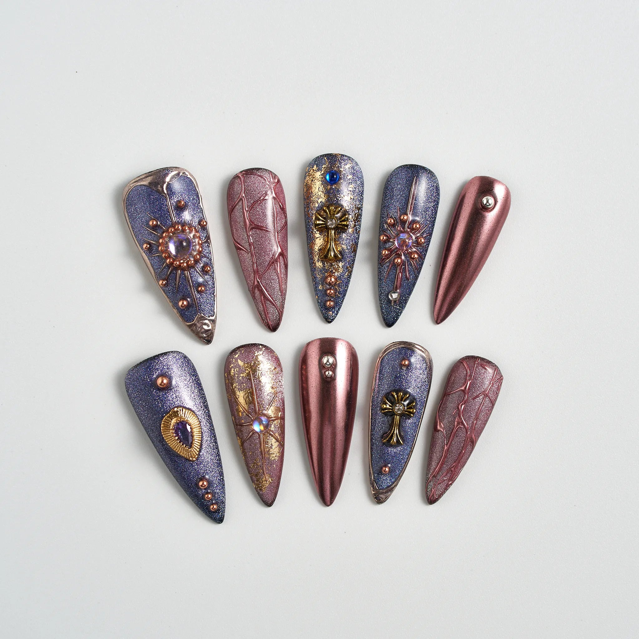 Decorative nail art tips with metallic and gemstone designs on a light gray background