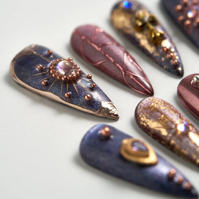 Decorative nail art with metallic and gemstone accents on a light background