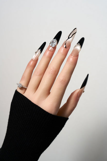 Zircon Eclipse reusable stiletto press-on nails featuring a striking black and nude asymmetrical design with large focal zircon crystals, black French tips, and delicate 3D swirl line art.