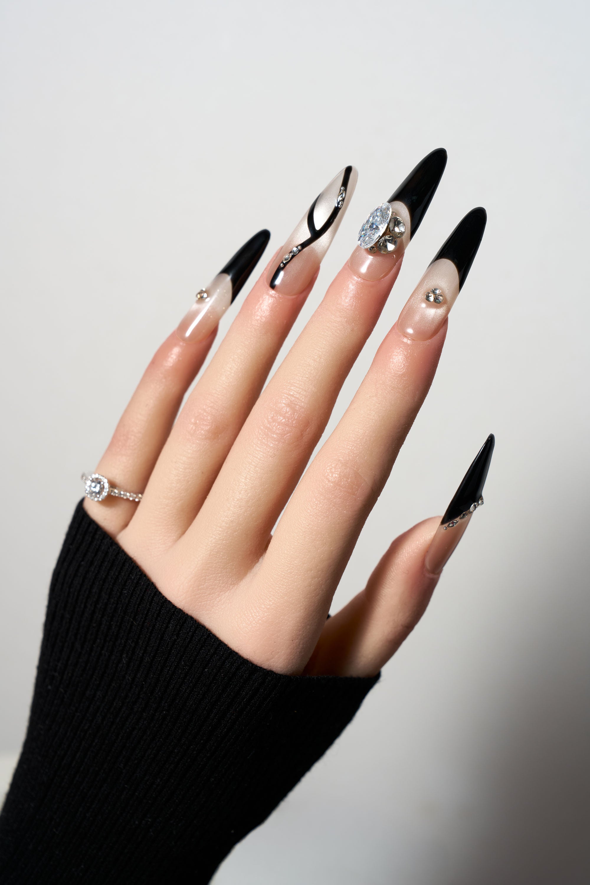 Zircon Eclipse reusable stiletto press-on nails featuring a striking black and nude asymmetrical design with large focal zircon crystals, black French tips, and delicate 3D swirl line art.